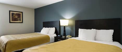 A hotel room with two beds, each with a yellow bedspread, a bedside table with a lamp, and a framed picture on the wall.
