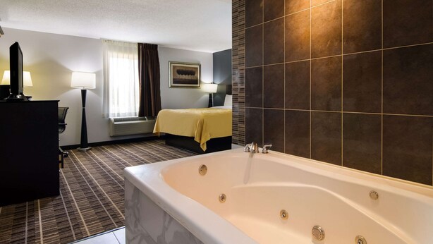 Une chambre d’hôtel avec une grande baignoire, un lit recouvert d’une courtepointe jaune, un bureau avec une lampe et une fenêtre avec des rideaux.