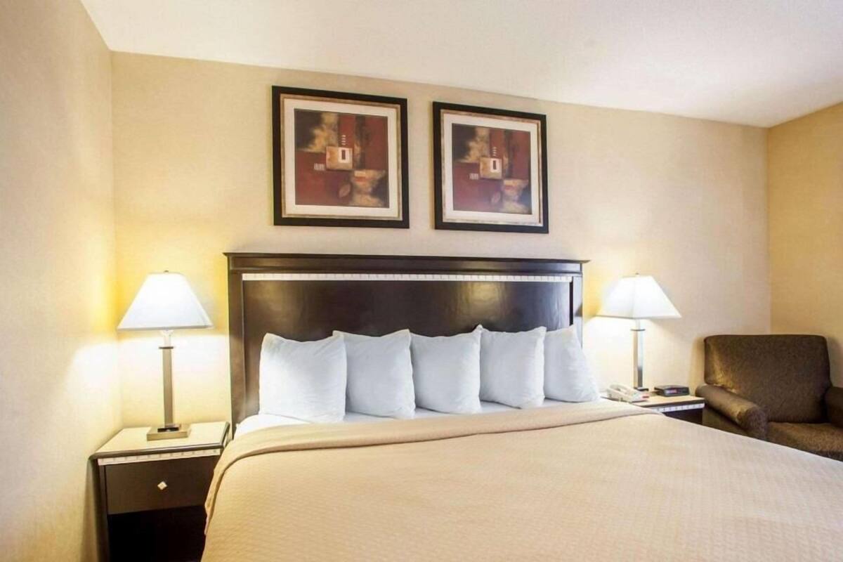 A hotel room with a large bed, two bedside lamps, a chair, and two framed pictures on the wall.