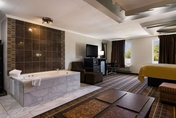 A modern hotel room with a marble bathtub, a flat-screen TV, a desk, a comfortable armchair, and a large bed.