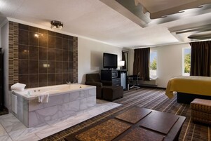 Una habitación de hotel moderna con una bañera de mármol, un televisor de pantalla plana, un escritorio, un sillón cómodo y una cama grande.