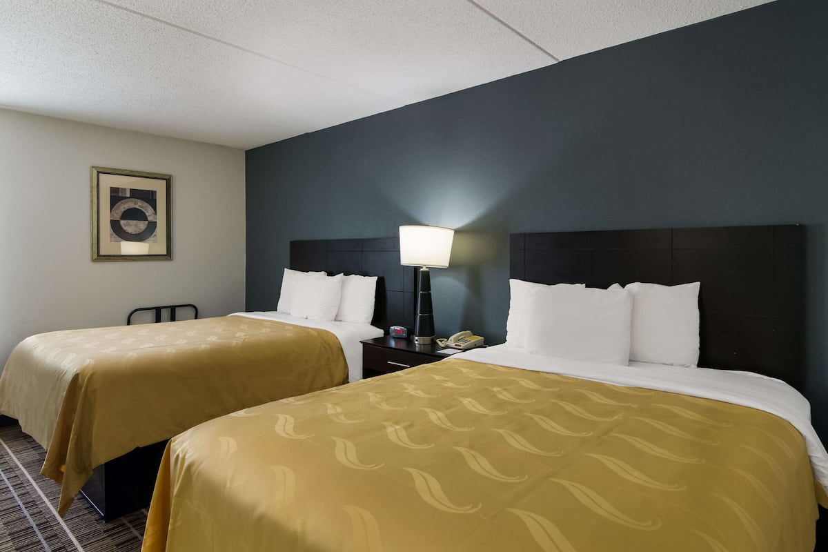 A hotel room with two beds, a nightstand with a lamp, a telephone, and a framed picture on the wall.