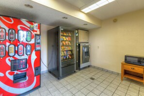 A vending machine with a Coca-Cola logo, a refrigerator with snacks, and a microwave on a wooden table. - Red Roof Inn Memphis East (Memphis)