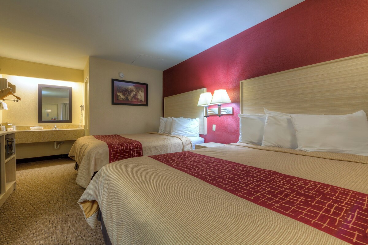 A hotel room with two beds, a bathroom, and a red accent wall.