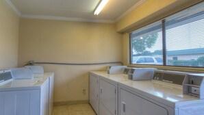A laundry room with two front-loading washing machines, a dryer, and a window with blinds. - Red Roof Inn Memphis East (Memphis)