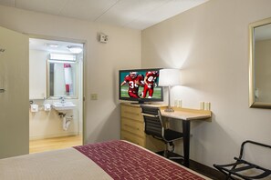 A hotel room with a bed, a desk with a chair, a television displaying a sports game, a lamp, and a mirror on the wall. - Red Roof Inn Memphis East (Memphis)