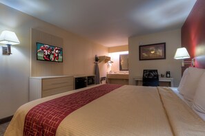 A hotel room with a bed, a television mounted on the wall, a desk with a chair, a mirror, and a window. - Red Roof Inn Memphis East (Memphis)