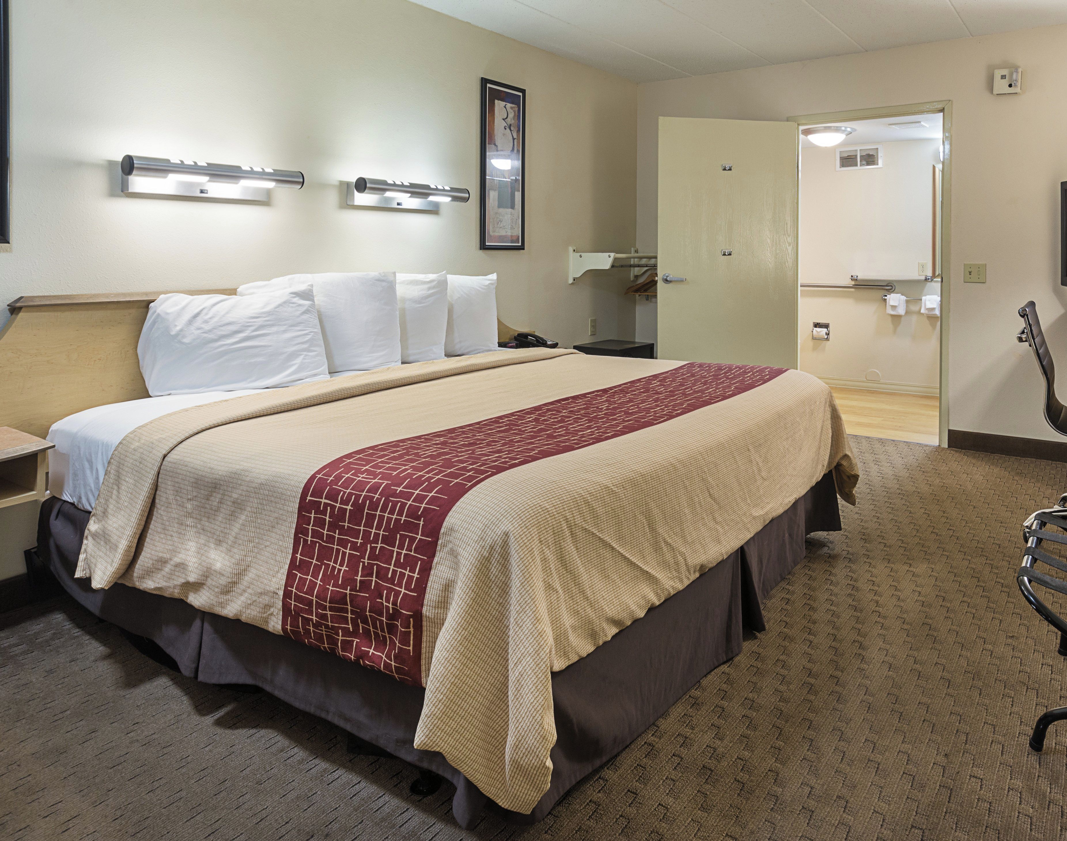 A hotel room with a bed, bedside tables, a mirror, and a door leading to a bathroom.