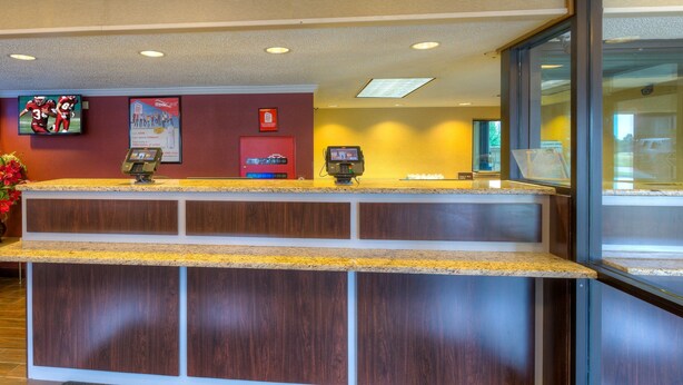 A reception desk with a digital kiosk, a red door, and a poster on the wall. - Red Roof Inn Memphis East (Memphis)