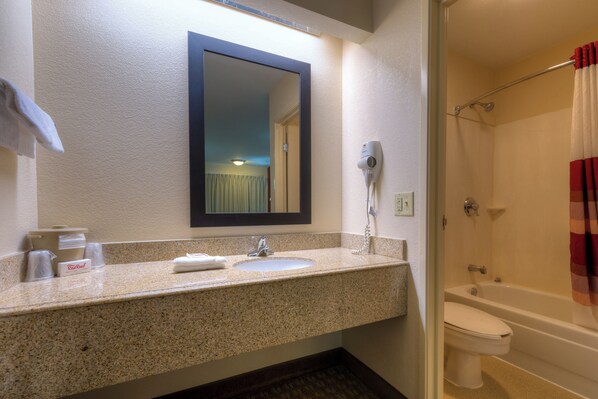 Baño con encimera de granito, lavamanos, espejo, secador de pelo y ducha con cortina.