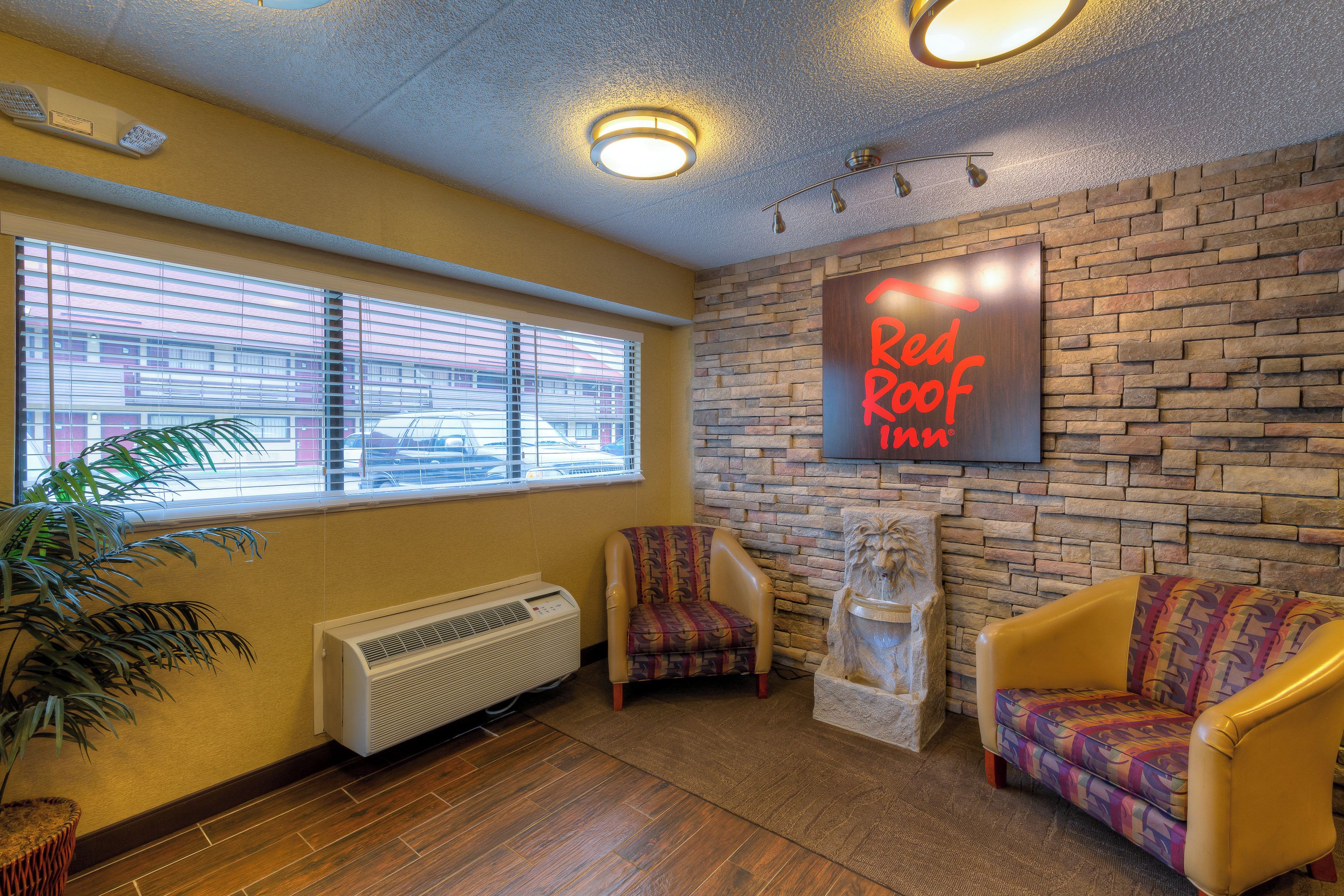 A room with a brick wall, two patterned armchairs, a radiator, and a window with blinds.