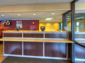 A hotel reception desk with a digital kiosk, a red door, and a large window. - Red Roof Inn Memphis East (Memphis)