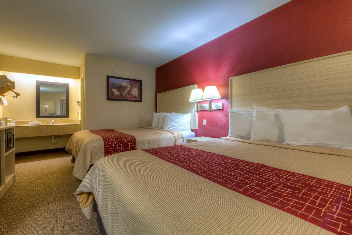 A hotel room with two beds, a bathroom, and a red accent wall.