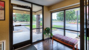 A hotel lobby with a bench, large windows, and a door leading outside. - Red Roof Inn Memphis East (Memphis)