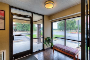 A hotel lobby with a bench, large windows, and a door leading outside. - Red Roof Inn Memphis East (Memphis)