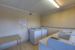 A laundry room with a washing machine, dryer, and a table. There are signs on the wall indicating laundry detergent and fabric softener availability.