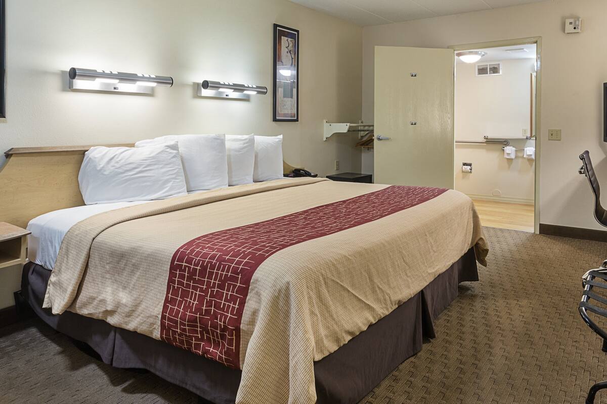 A hotel room with a bed, bedside tables, a mirror, and a door leading to a bathroom.