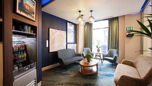 A hotel room with a seating area, a refrigerator stocked with beverages, and artwork on the walls. - Thistle London Piccadilly (London)