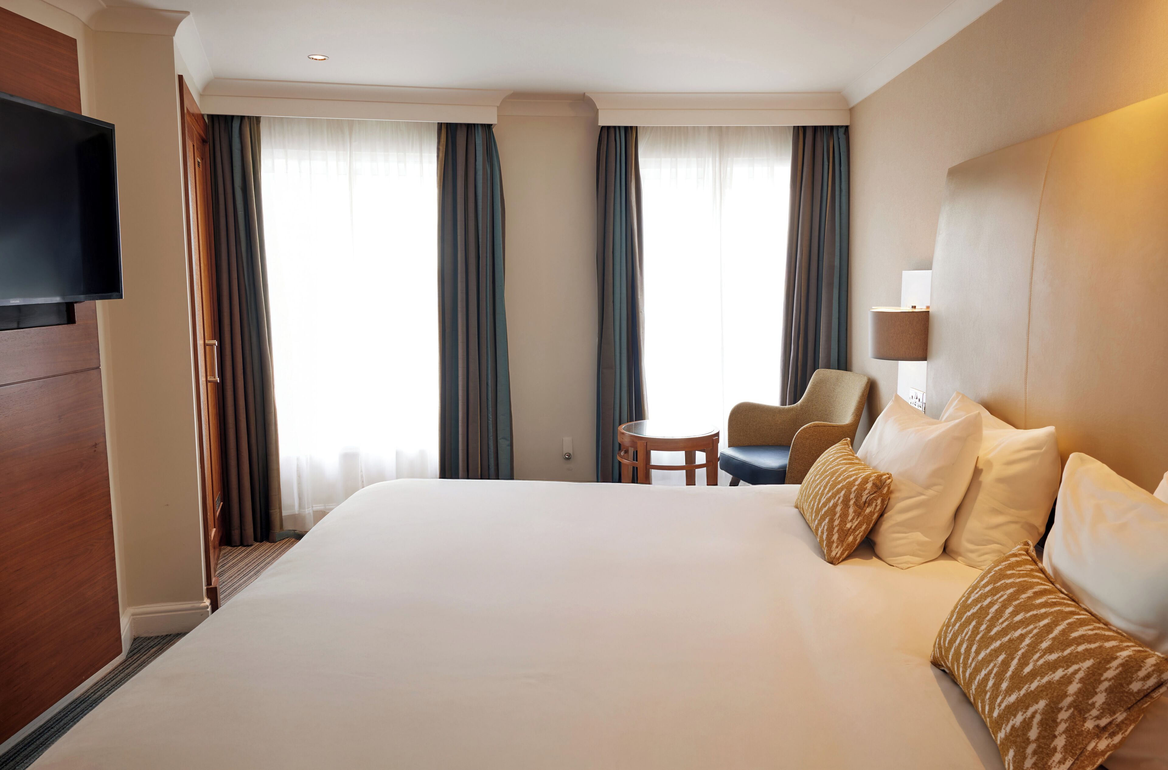 A hotel room with a large bed, a television mounted on the wall, a small round table, and two chairs.