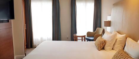 Una habitación de hotel con una cama grande, un televisor en la pared, una mesita redonda y dos sillas.