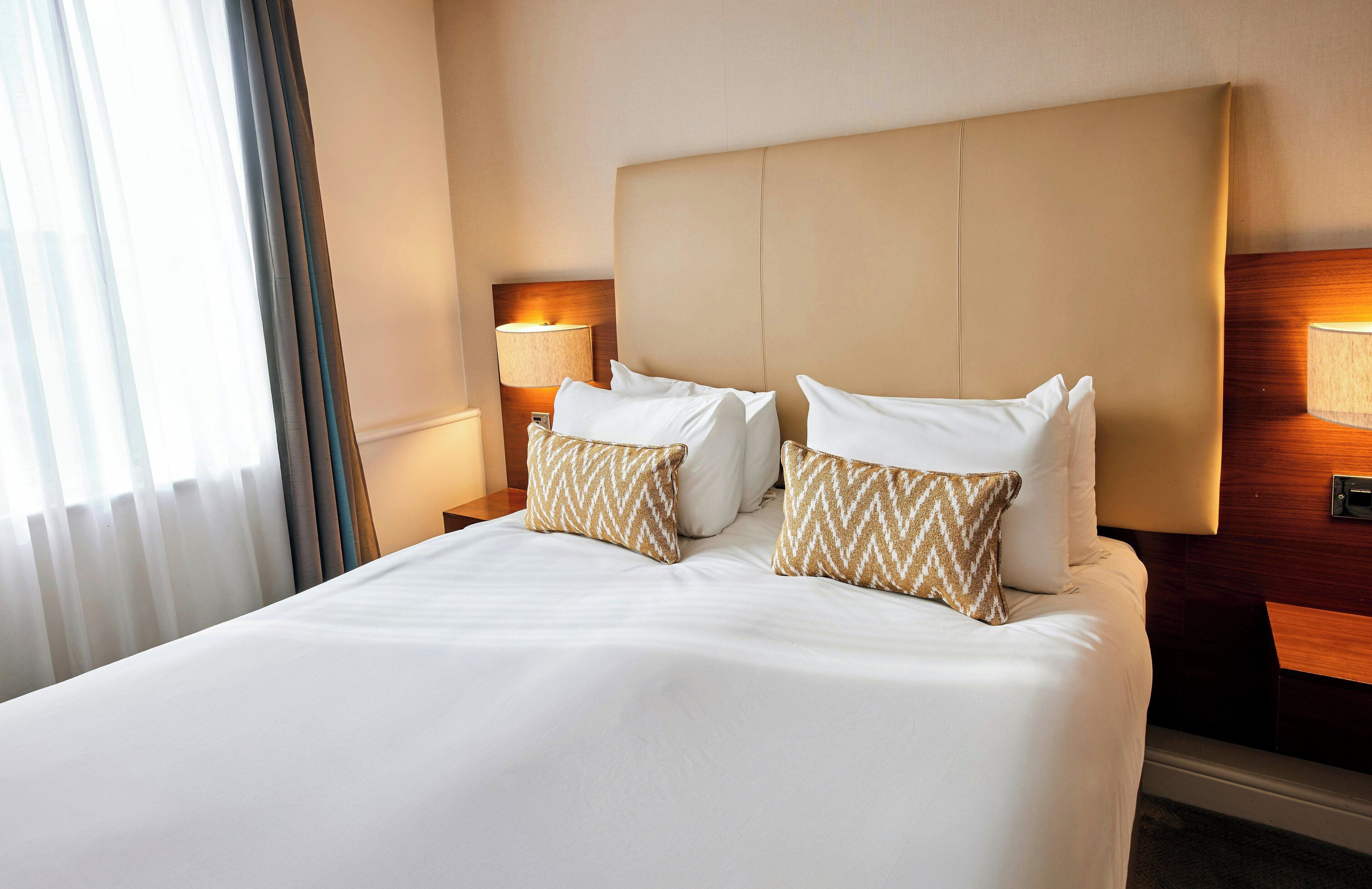 A hotel room with a large bed, two bedside lamps, and a headboard.