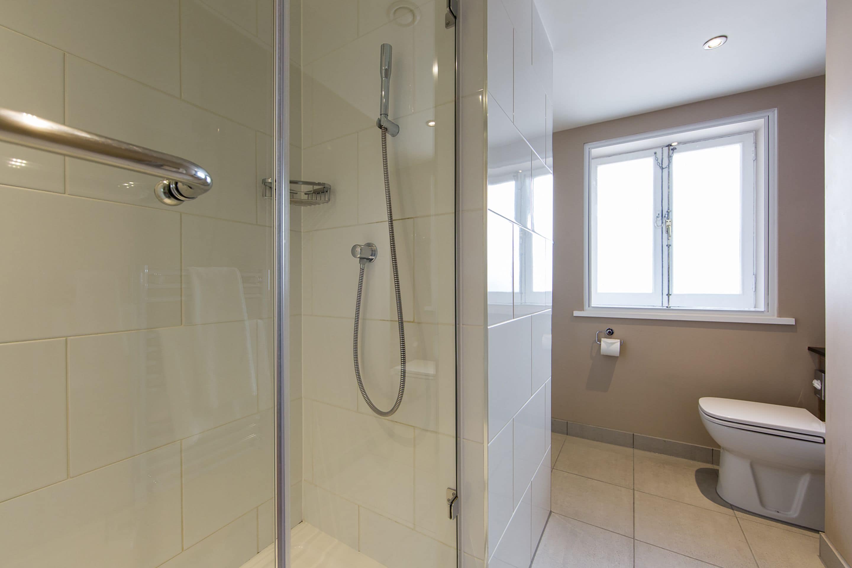 Een moderne badkamer met een douchecabine van glas, een toilet en een raam voor natuurlijk licht.