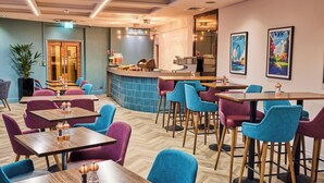 A restaurant with multiple tables and chairs, a bar area, and a kitchen visible through an open doorway. - Thistle London Piccadilly (London)