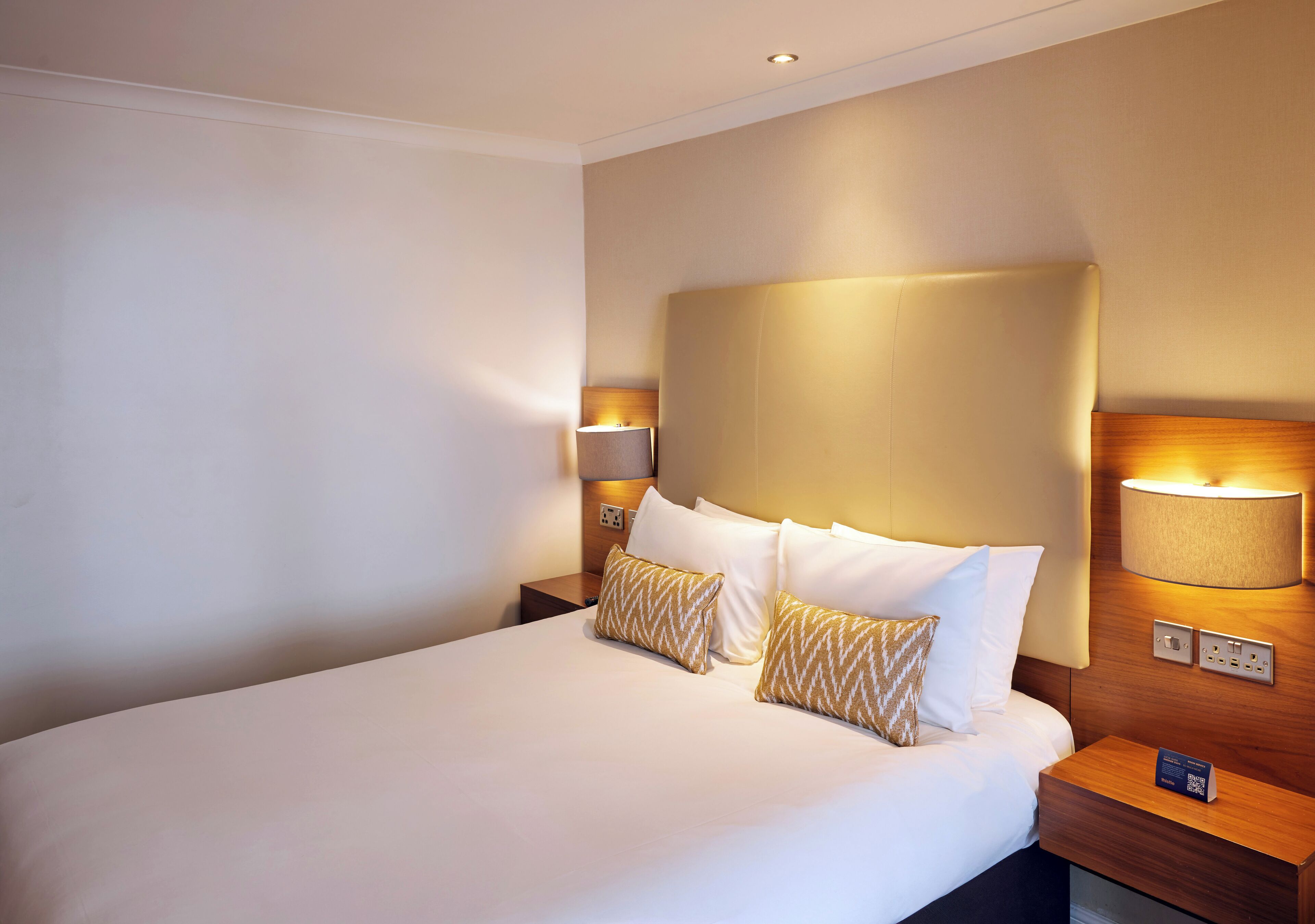 A hotel room with a large bed, two bedside lamps, and a nightstand with a lamp.