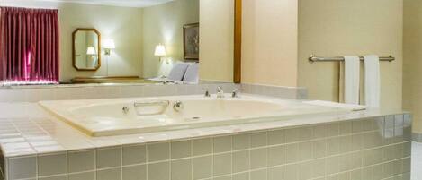 A hotel bathroom with a large bathtub, a mirror, a towel rack, and a toilet.