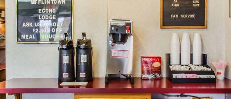 A reception desk with a welcome sign, a framed certificate, a coffee machine, and a menu board.