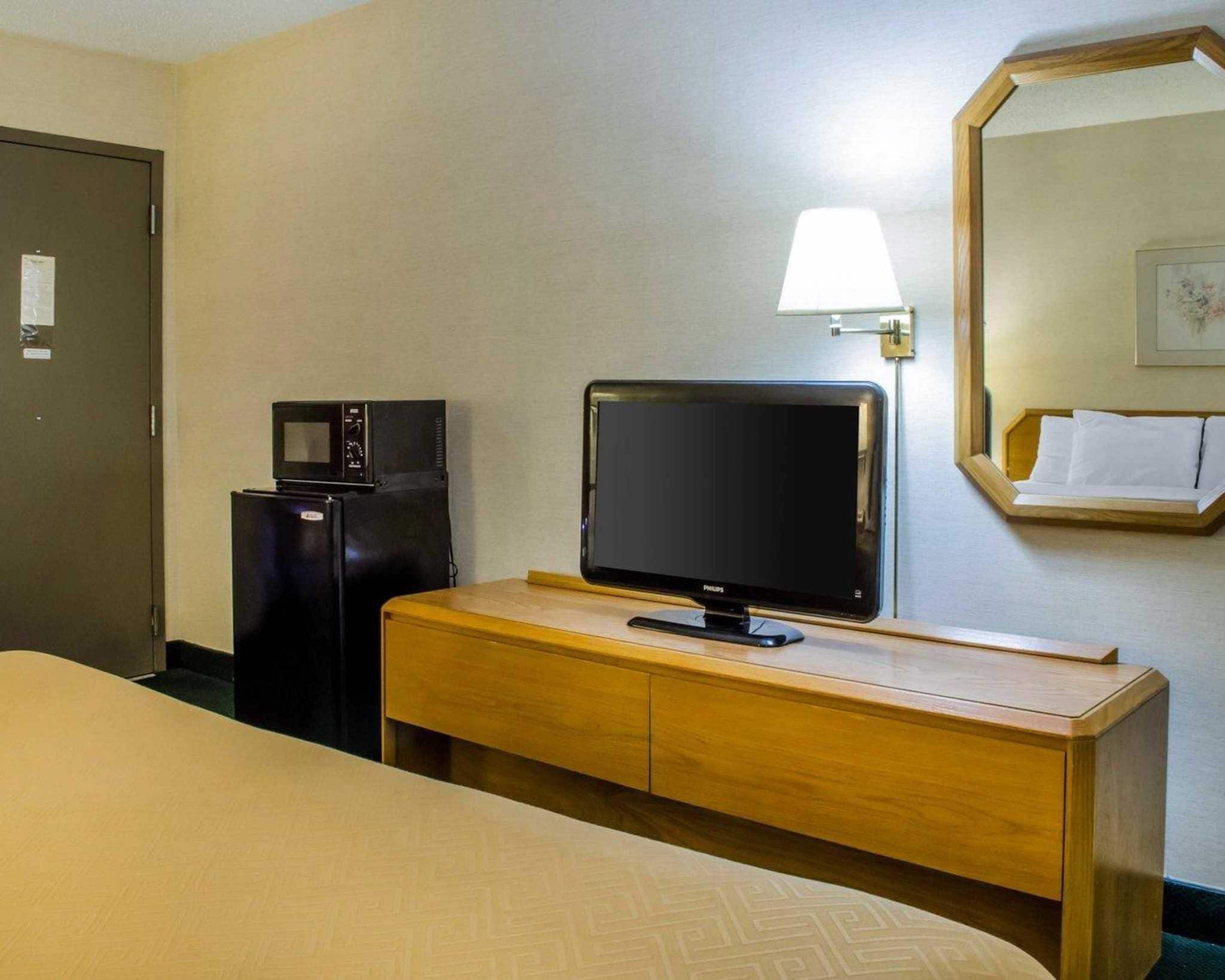Ett hotellrum med en säng, en byrå i trä, en tv, en mikrovågsugn och en spegel.