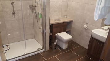 A bathroom with a glass shower enclosure, a toilet, a sink, and a wooden vanity.