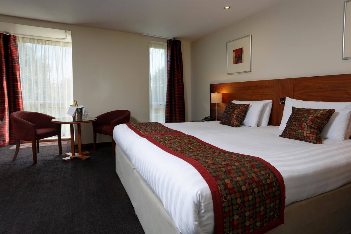 A hotel room with a large bed, two chairs, a small table, and a nightstand.