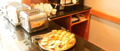 Un buffet de petit-déjeuner comprenant une machine à café, un grille-pain et une variété de viennoiseries, le tout disposé sur un comptoir noir.