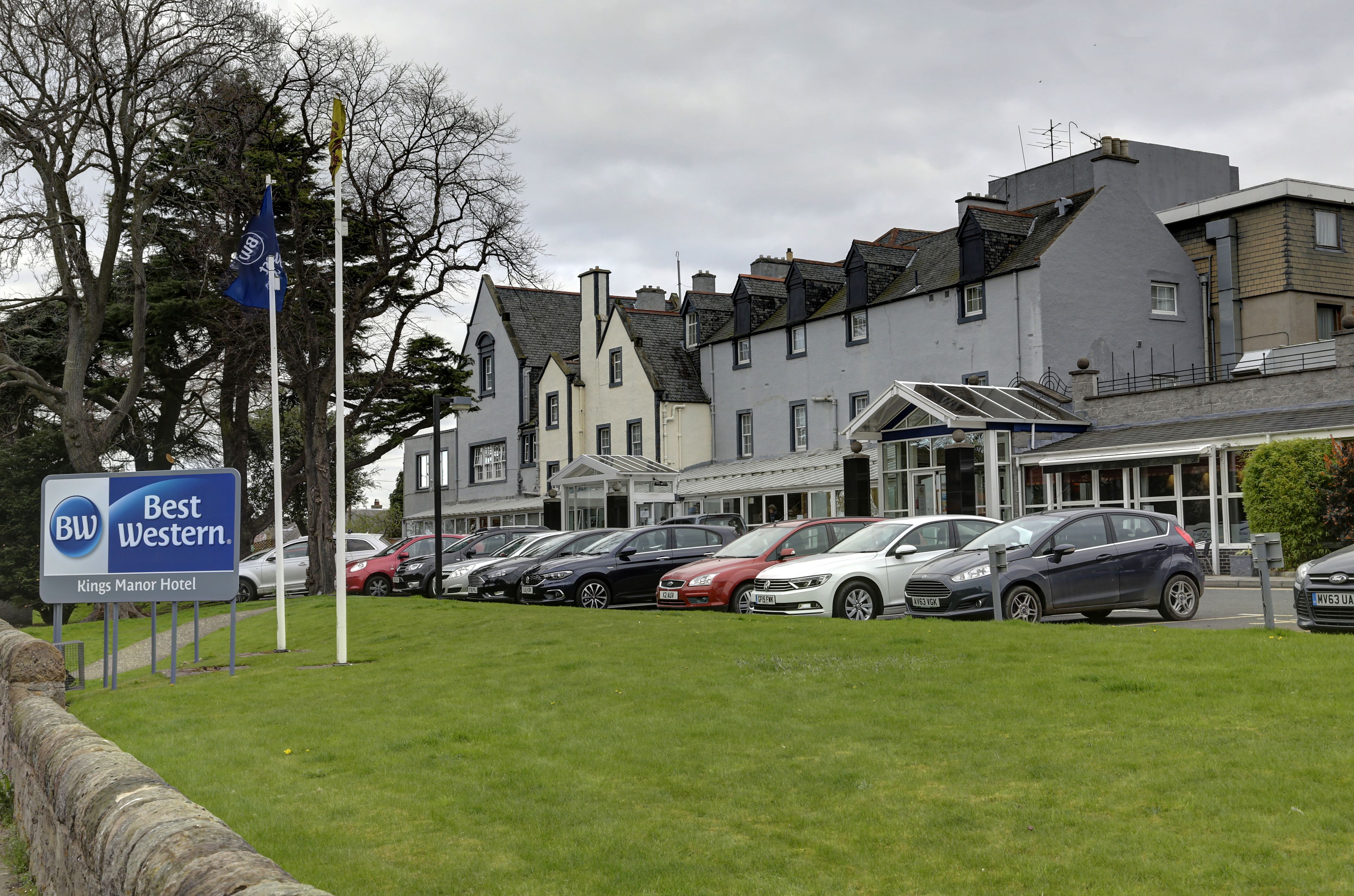 A hotel with a sign reading "Best Western Kings Manor Hotel" and a parking lot with several cars.