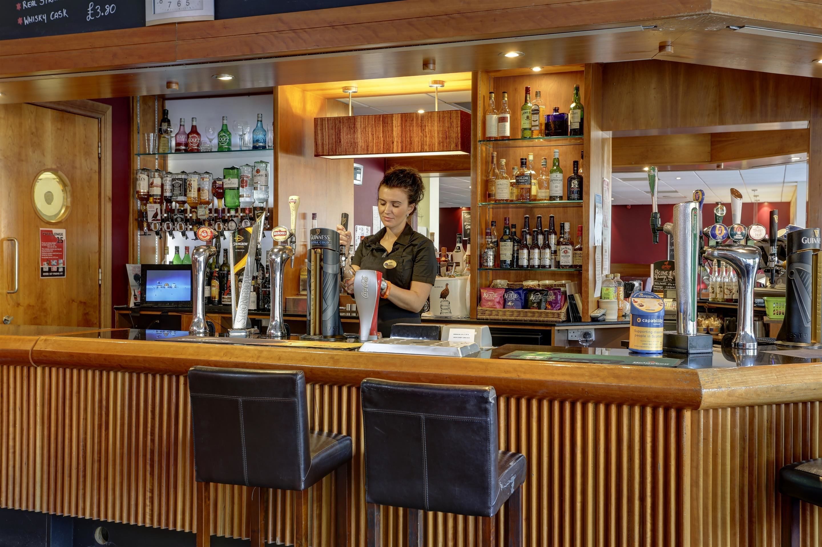 Zona de bar con un cantinero, diversas botellas de licores y una caja registradora.