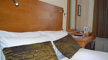 A neatly made bed with white and brown bedding, a wooden headboard, a bedside table with a lamp, and a mirror on the wall.