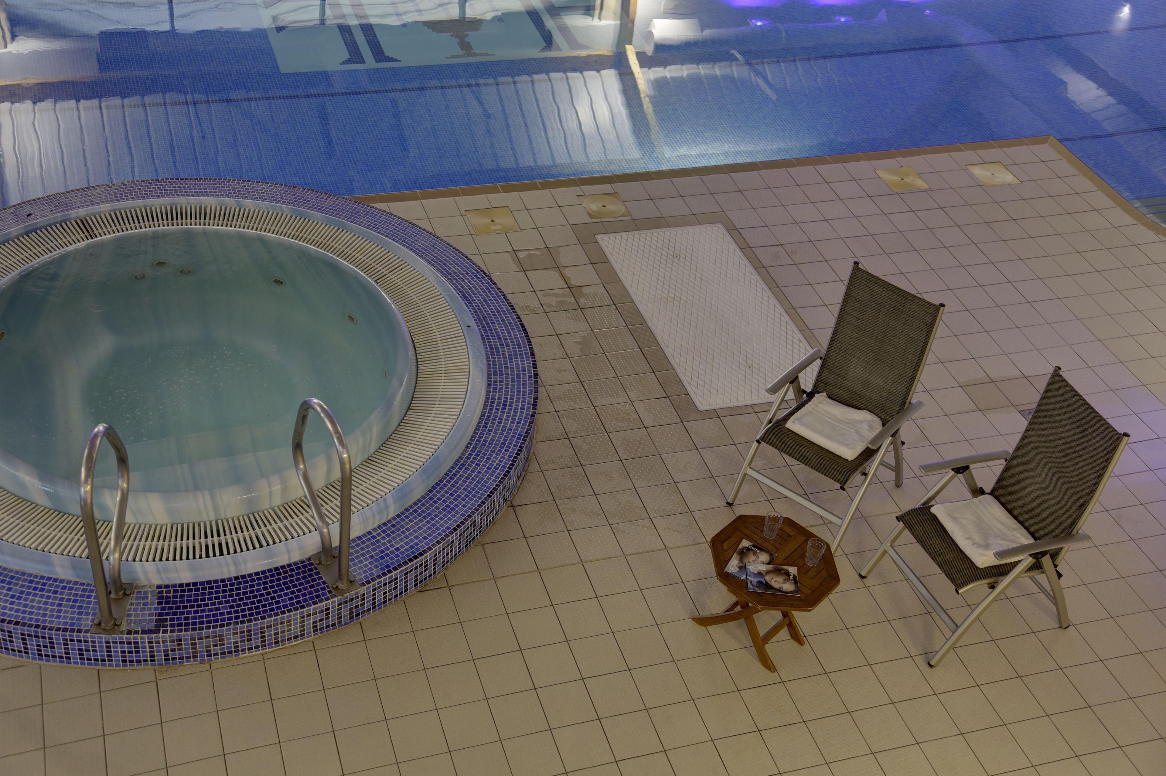 A pool area with a hot tub, lounge chairs, and a small table with a cat.