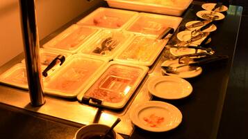 Un buffet avec plusieurs points de service, comprenant des plateaux et des bols remplis de nourriture, des ustensiles et des assiettes.