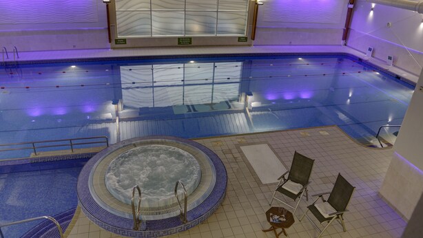 An indoor swimming pool with a hot tub, lounge chairs, and a tiled floor.