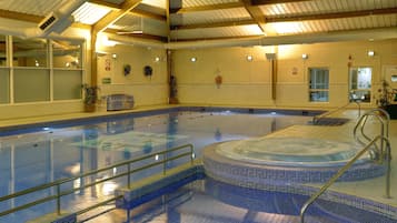 An indoor swimming pool with a hot tub, glass railings, and a tiled floor.