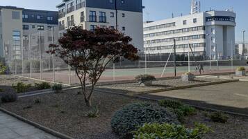 Un cortile con un campo da tennis, circondato da edifici con balconi e una torre di controllo.