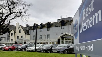 A hotel sign with "Best Western" and "Kings Manor Hotel" text, parked cars, and traditional buildings in the background.