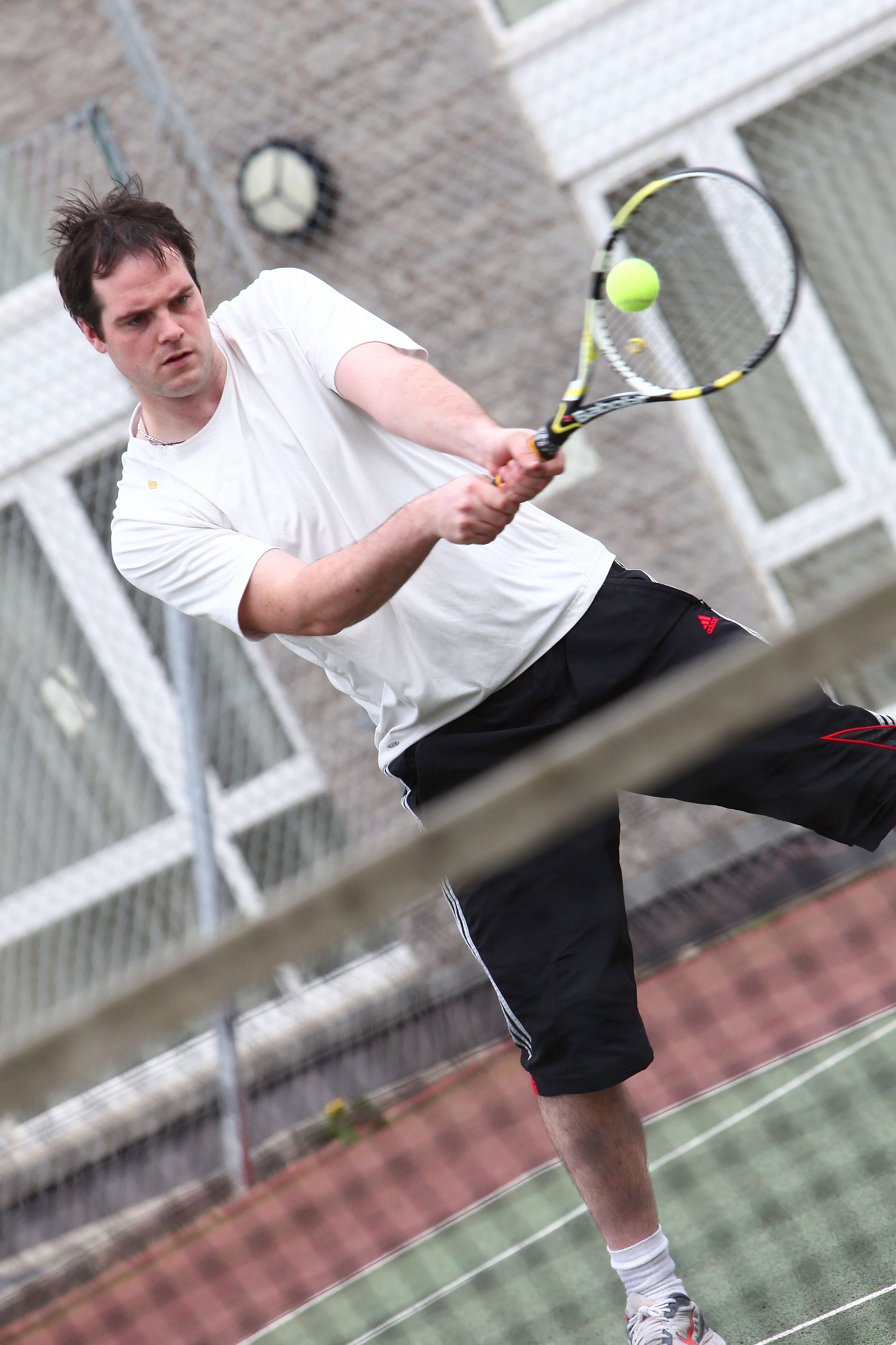 A tennis player in a white shirt and black shorts playing tennis.