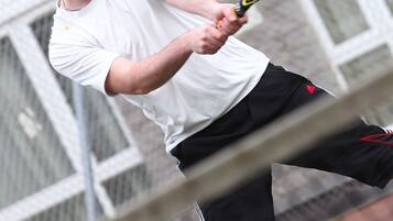 Un tenista con camisa blanca y pantones negros jugando al tenis.