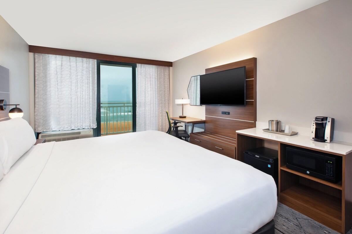 Een hotelkamer met een groot bed, een bureau met een flatscreen televisie, een koffiezetapparaat en een magnetron.