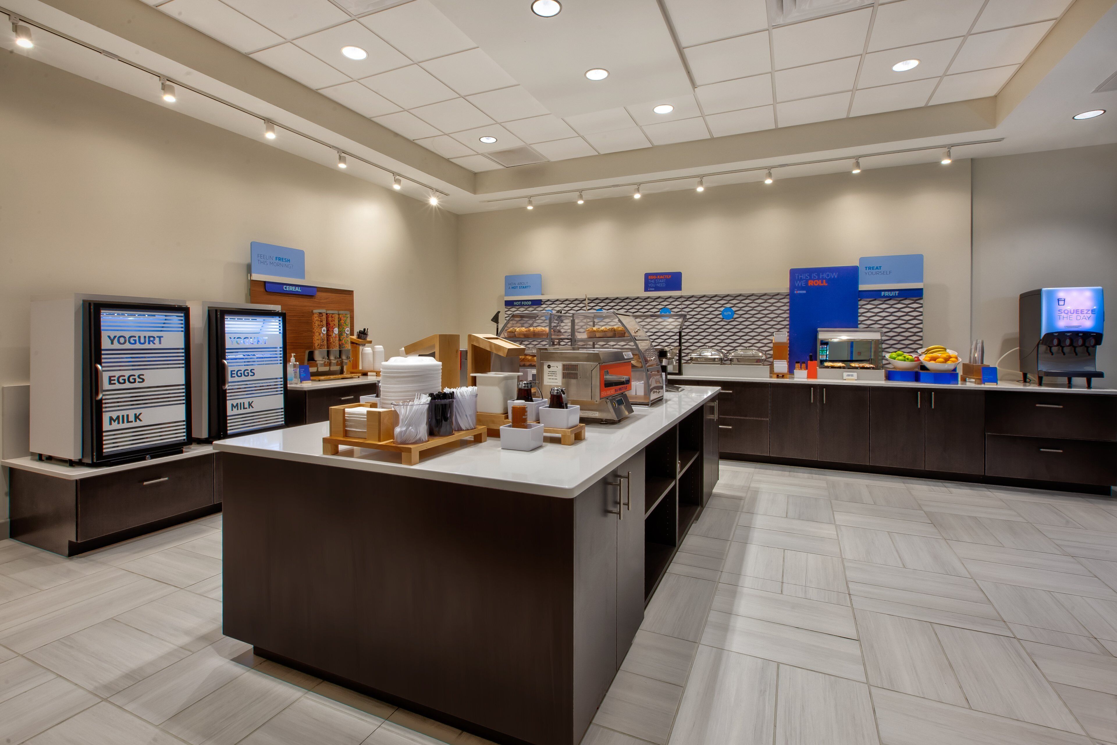 A modern breakfast area with self-serve stations for yogurt, eggs, and milk, a coffee machine, and a fruit display.