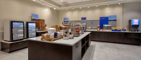 A modern breakfast area with self-serve stations for yogurt, eggs, and milk, a coffee machine, and a fruit display.