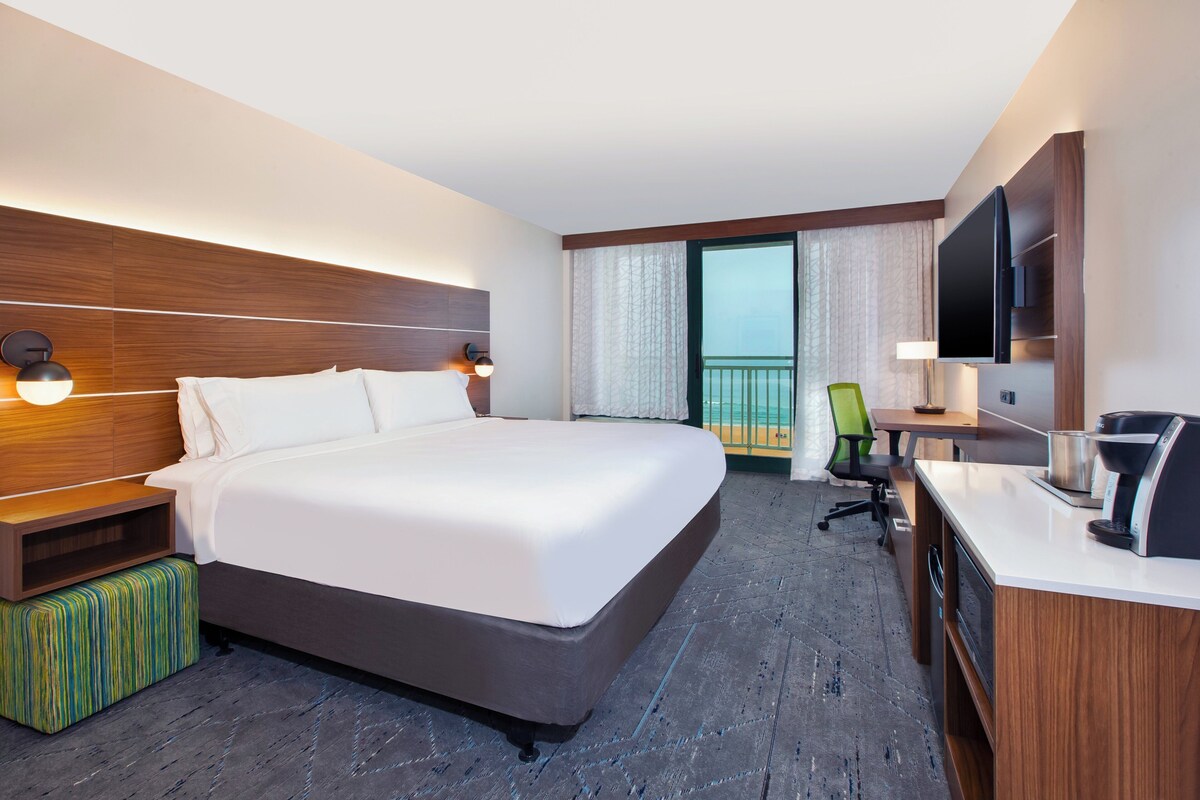 Een hotelkamer met een groot bed, een bureau met een koffiezetapparaat, een televisie en een balkon met uitzicht.
