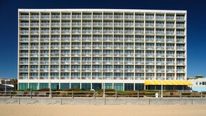 A multi-story hotel with a uniform balcony design, located near a sandy beach. - Holiday Inn Express & Suites VA Beach Oceanfront by IHG (Virginia Beach)